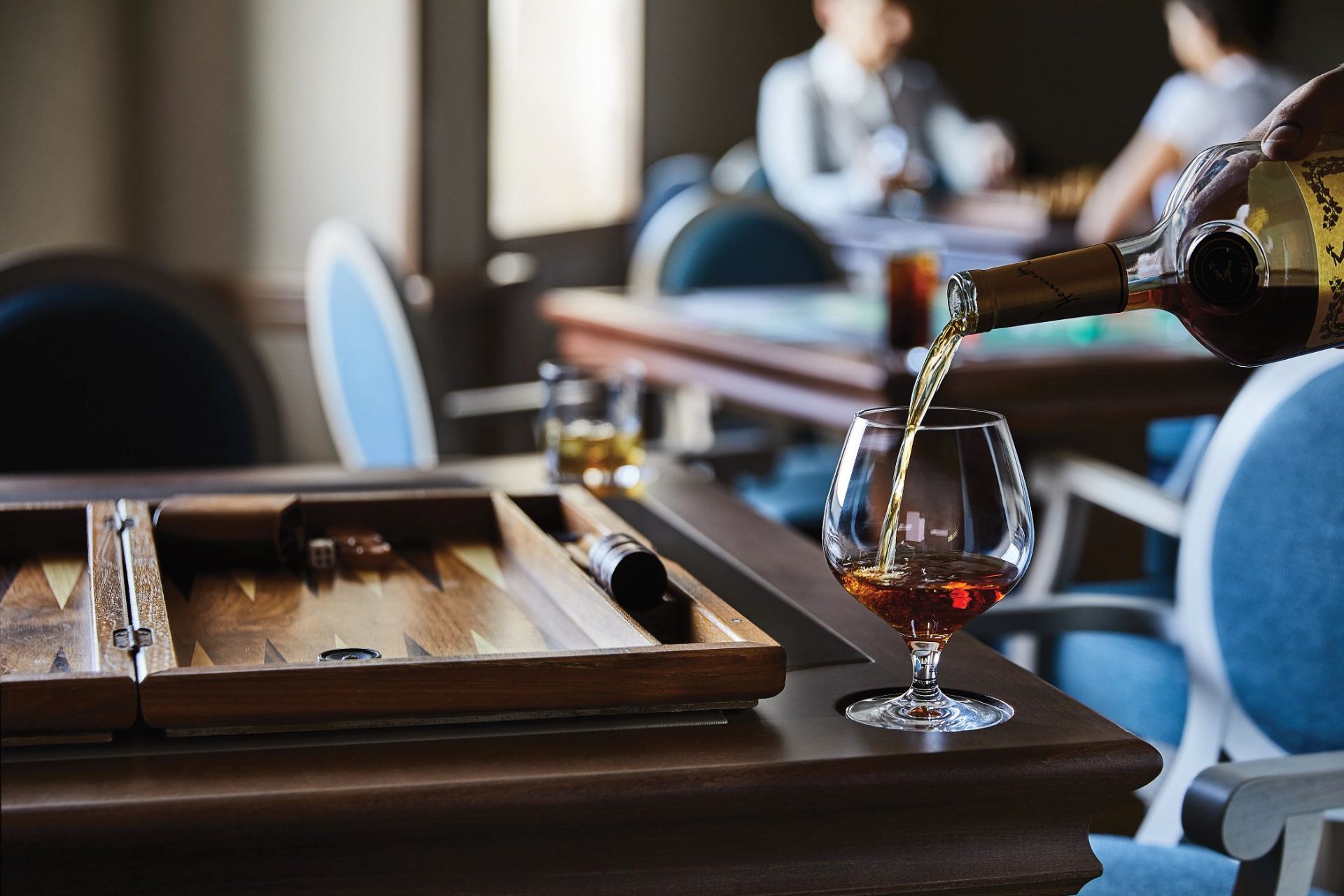 Cognac being poured in a quiet lounge with backgammon board